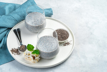 A natural, healthy dessert with chia seeds and coconut milk on a gray background with flowers, a napkin and space to copy. Side view.