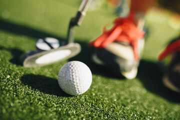 Kids play mini golf. Close-up image of player in snickers with mini golf club and white golf ball....