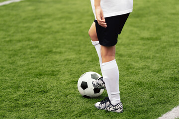 Soccer Player With White and Black Football Ball. Young Athlete Kicking Ball on Grass Field. Boy in White Soccer Jersey Uniform Kicking Ball