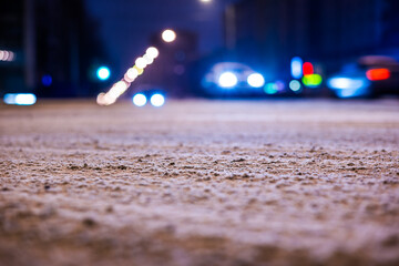 Winter night in the big city, the headlights of the approaching cars. Close up view of snow on the asphalt level