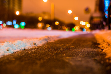 Winter night in the big city, the snow-covered street with a cleared path. Close up view from the asphalt level