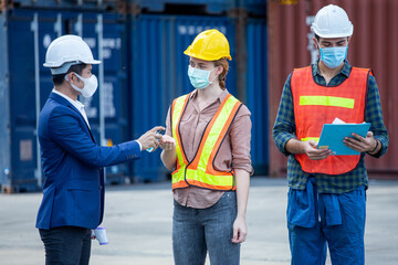 manager wear face mask scanning body temperature and using hand sanitizer alcohol gel to worker before entering working over Containers box at logistic Cargo during Coronavirus or Covid 19 pandemic