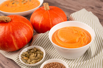 Hokkaido pumpkin cream soup in white bowl toped with pumpkin seeds on wooden table background with copy space for text. Vegan food concept, homemade soup recipe. Selective focus