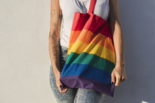 Curly-haired Spanish Cute Woman With A Pride Flag Tote Bag And Tattoos On A White Wall Background