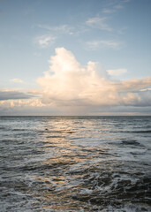 Fototapeta premium Beautiful golden light reflecting from clouds over the sea lighting up ocean waves on horizon and water with creamy gold tranquil colours on the coast.