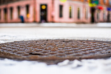 Snowy winter in the big city, the city street. Close up view of a hatch at the level of the asphalt