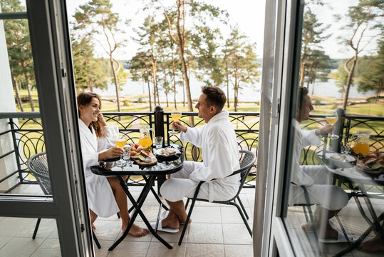 A couple in love sitting on the balcony of a hotel room in their bathrobes and having breakfast