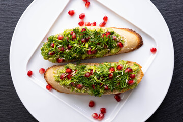 two snacks - avocado, sprinkled with ripe pomegranate seeds, sesame seeds and fresh dill, lie on a white plate
