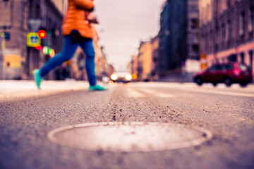 Snowy winter in the big city, a pedestrian crossing the road in front of riding car. Close up view of a hatch at the level of the asphalt