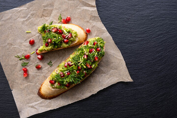 on parchment paper there is one bitten and one whole snacks made of avocado, pomegranate and dill seeds