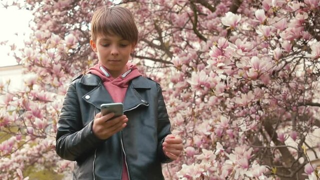 The boy moves to the music from the smartphone. Technology improvements have changed the way we listen to musical works outdoors. Spending time outside. 