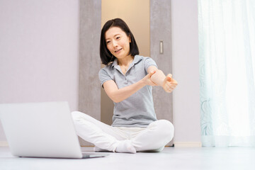 Fototapeta na wymiar パソコンを見ながら軽い運動をする女性（40代、50代イメージ）