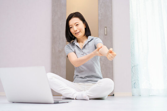 パソコンを見ながら軽い運動をする女性（40代、50代イメージ）