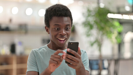 Young African Man Celebrating Success on Smartphone