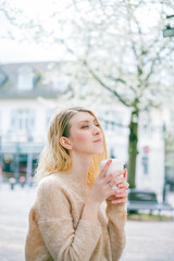 Beautiful young woman drinks coffee to go on the street of a European city. Happiness. Spring.