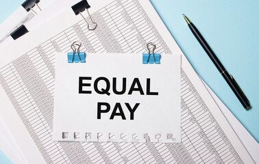On a light blue background, documents, a pen and a sheet of paper on blue paper clips with the text EQUAL PAY. Business concept.