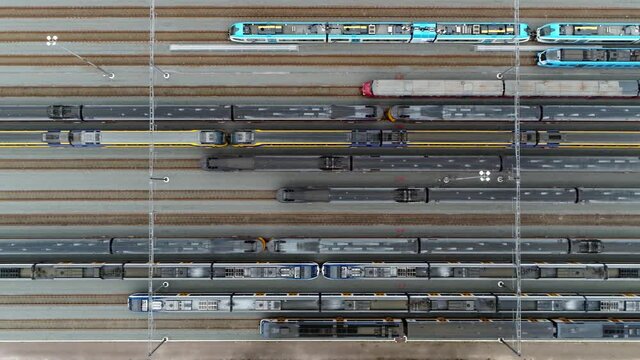 Aerial top down view of trains parked at a service station that run along a railroad track to transport passengers showing lots of tracks straight next to each other and the railway cars 4k quality