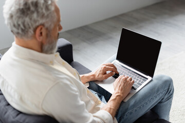 blurred man typing on laptop while sitting on couch at home.