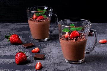 Chocolate mousse topped with strawberry and mint in irregular glass cup on the gray table. Whipped exquisite dessert