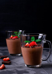 Chocolate mousse topped with strawberry and mint in irregular glass cup on the gray table. Whipped exquisite dessert