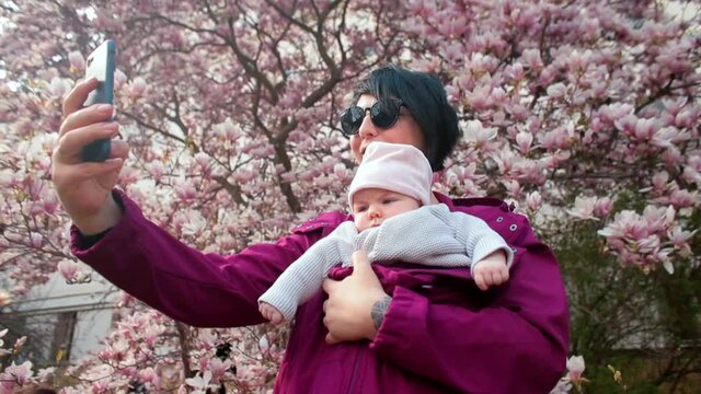 Spring photo session of a mother with a child using the mobile photography app. She select the portrait shooting mode, take a selfie and use the frontal camera of smartphone. 