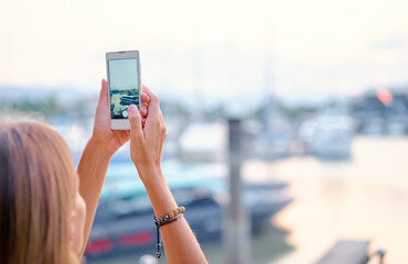 Tourism concept. Young woman taking photo on smartphone while standing on the harbor seafront.
