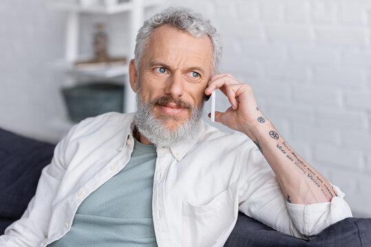 Tattooed And Bearded Man With Grey Hair Talking On Mobile Phone.