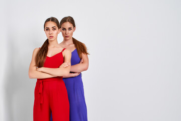 Naklejka premium Two girls standing in studio in elegant colorful overalls on white background