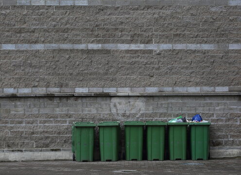 Six Mobile Plastic Green Dumpsters Against The Gray Wall