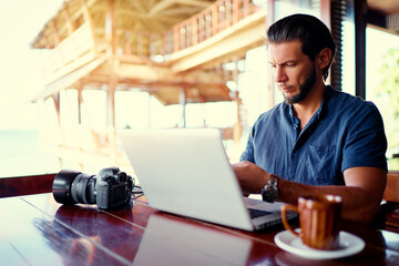 Fototapeta premium Freelance concept. Young bearded man working on laptop computer while sitting on cafe terrace.