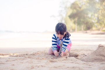7 years old asian girl play sculpture white sand on the sea beach.Vacation and relax.Playful active kid on beach in summer vacation and child development.Asian kid girl play in sand beach in thailand.