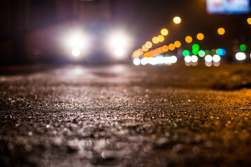 Rainy night in the big city, glare from the headlights of the parked car. Close up view from the...