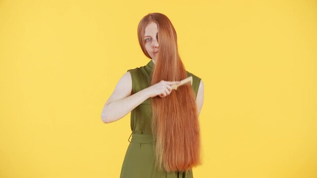 Portrait of woman with freckles on face brushing her long beautiful ginger hair and looking into the camera. Yellow background