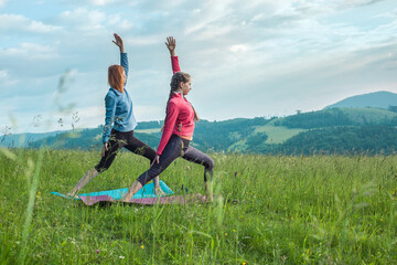 Yoga in nature, fresh air in park. Group of sporty women practicing pose together, stretching health on top of mountain in meadow at sunrise, zen wellness. Teamwork, good mood life.
