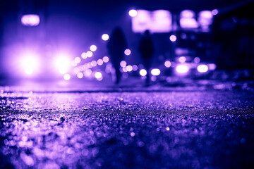 Rainy night in the big city, glare from the headlights of the car parked and people passing near....