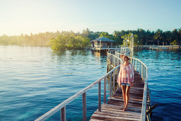 Vacation on tropical island. Young woman in hat enjoying sunset sea view from wooden bridge terrace, Siargao Philippines.