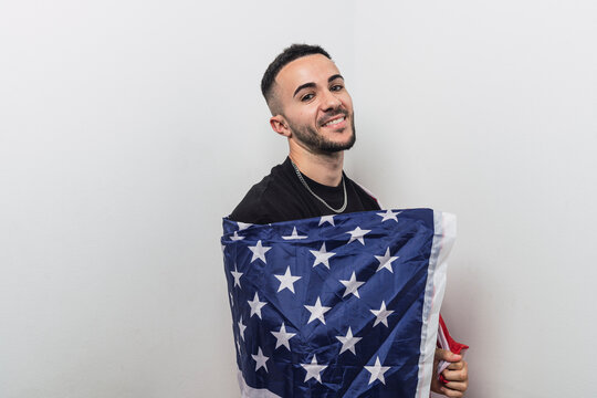 Chico joven atractivo sujetando una bandera de estados unidos delante una pared blanca