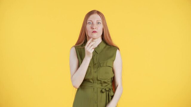 Young woman with freckles and long ginger hair is blowing out cheecks, looking into the camera and up and making "shhh" gesture. Then she disapperas. Yellow background