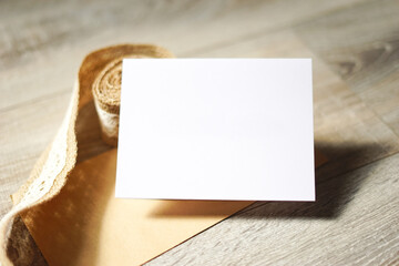Blank white card on wooden background with a natural paper envelope and burlap ribbon. Empty space for text. Copy space.