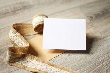 Blank white card on wooden background with a natural paper envelope and burlap ribbon. Empty space for text. Copy space.