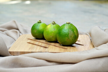 three limes (Citrus × aurantiifolia) on a wooden tray. commonly used in tropical restaurants with hot weather good for detoxification. close up view with selective focus