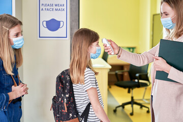 Side view of teacher checks temperature of students at school