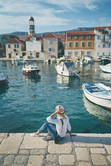 Fototapeta na wymiar Tourism concept. Young traveling woman enjoying the view of Kastel Castle sitting near the sea on Croatian coast.