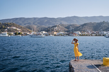 Fototapeta na wymiar Traveling by Greece. Young happy woman enjoying the view of Poros bay on the sea promenade.