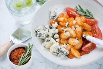 Plate of potato gnocchi served with sun dried tomato pesto and gorgonzola, close-up on a light-grey marble surface