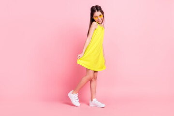 Full length photo of cute adorable school girl wear yellow dress dark eyewear smiling dancing isolated pink color background
