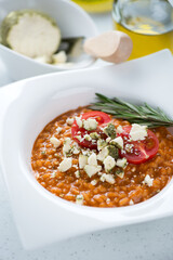 Close-up of risotto with sun dried tomato pesto and belper knolle served in a white plate, vertical shot, selective focus