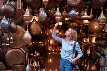 Keuken spatwand met foto Travel and shopping. Young traveling woman with choose presents in copper souvenir handicraft shop in Morocco. © luengo_ua