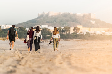 Friends walk on the beach on a sunny day. Back view. Castle and old town in the background.