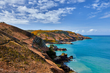 Image of Bouley Bay with the headland with a foot path in the foreground, Jersey CI, blue sky with cloud, at low tide.  Jersey, Channel Islands